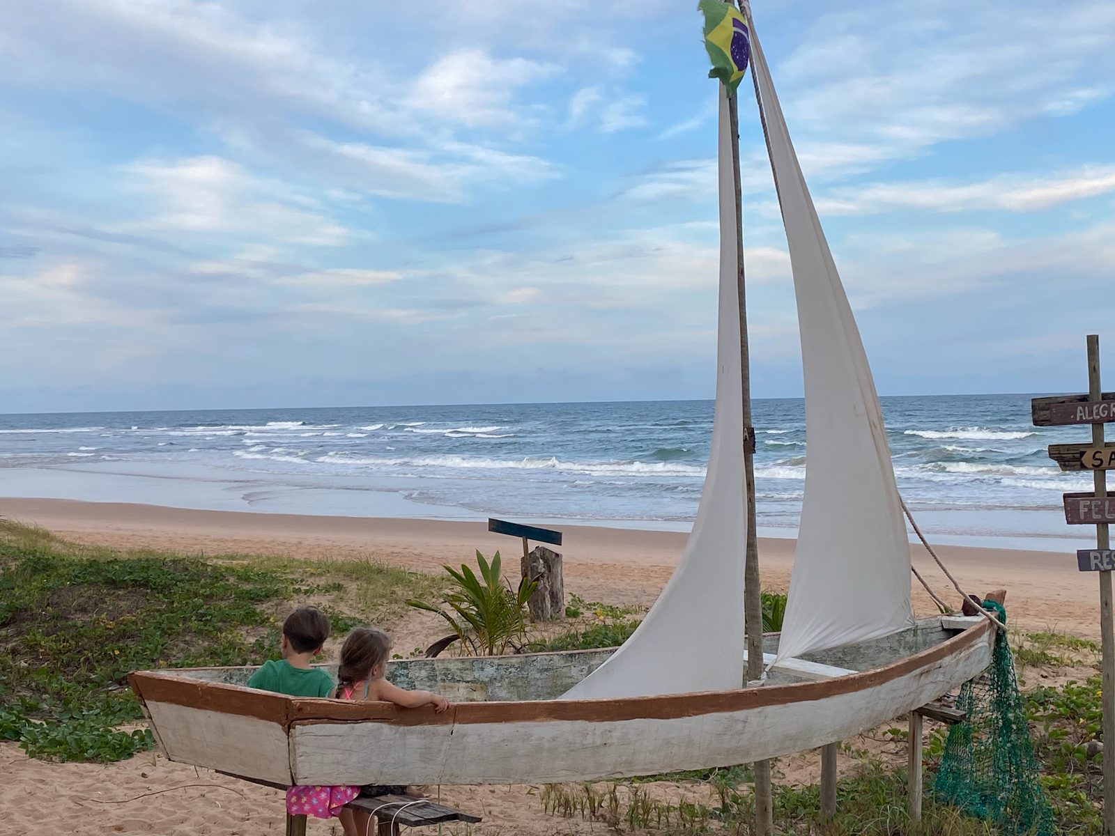 A child standing on a fishing boat beached on the shore, looking out to sea.