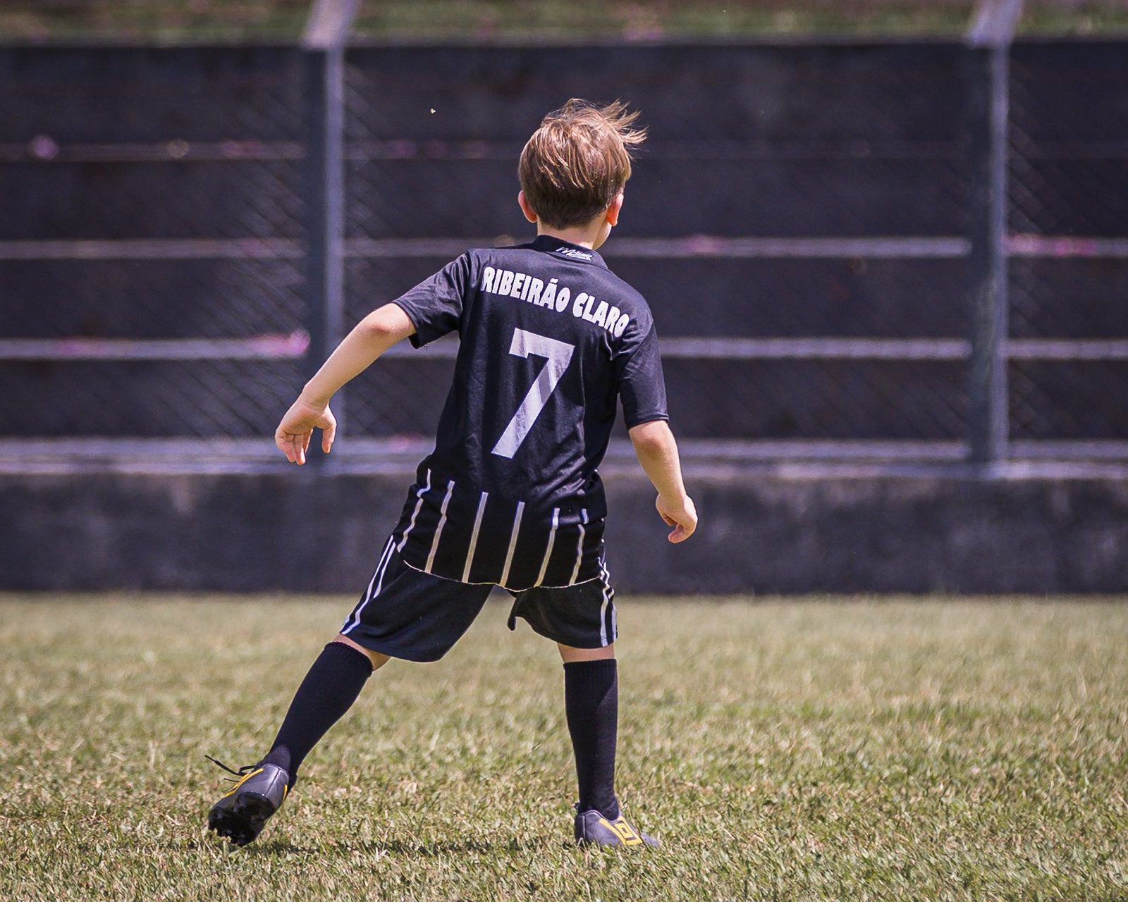 A young footballer in a number 7 shirt on the pitch in Ribeirão Claro, seen from behind.